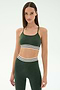 A woman wearing the SPLITS59 Cali Active Rib Bra in Heather Military with matching high-waisted leggings featuring white and black striped bands stands against a plain light background.