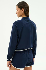 A person faces away, wearing the SPLITS59 Carrie Woven Nylon Jacket in Indigo/Lotus Red against a plain background.
