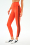 Model wears SPLITS59 Ella High Waist Airweight 7/8 leggings in Valencia/Indigo—orange with black side stripes—paired with white sneakers, standing against a plain white background.