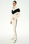 A person stands on a white background wearing the SPLITS59 Lottie Chevron Sherpa Full Zip Jacket in Creme/Black—crafted from 100% polyester with a black chevron stripe—paired with cream pants featuring black side stripes and cream sneakers.