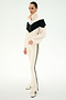 A person stands on a white background wearing the SPLITS59 Lottie Chevron Sherpa Full Zip Jacket in Creme/Black—crafted from 100% polyester with a black chevron stripe—paired with cream pants featuring black side stripes and cream sneakers.