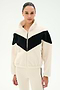 A woman stands against a plain white background wearing the SPLITS59 Lottie Chevron Sherpa Full Zip Jacket in creme and black, crafted from soft 100% polyester fabric, paired with cream pants featuring a black stripe.