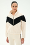 A woman stands against a plain white background wearing the SPLITS59 Lottie Chevron Sherpa Full Zip Jacket in creme and black, crafted from soft 100% polyester fabric, paired with cream pants featuring a black stripe.