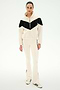 A woman stands against a plain white background wearing the SPLITS59 Lottie Chevron Sherpa Full Zip Jacket in Creme/Black, featuring a black chevron design and crafted from smooth polyester, paired with cream pants with black stripes and cream sneakers accented with black stripes.