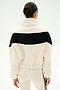 A person with dark hair in a bun models the SPLITS59 Lottie Chevron Sherpa Full Zip Jacket in Creme/Black—crafted from soft polyester fleece and featuring a black horizontal stripe—seen from the back, and paired with cream leggings that have black side stripes.