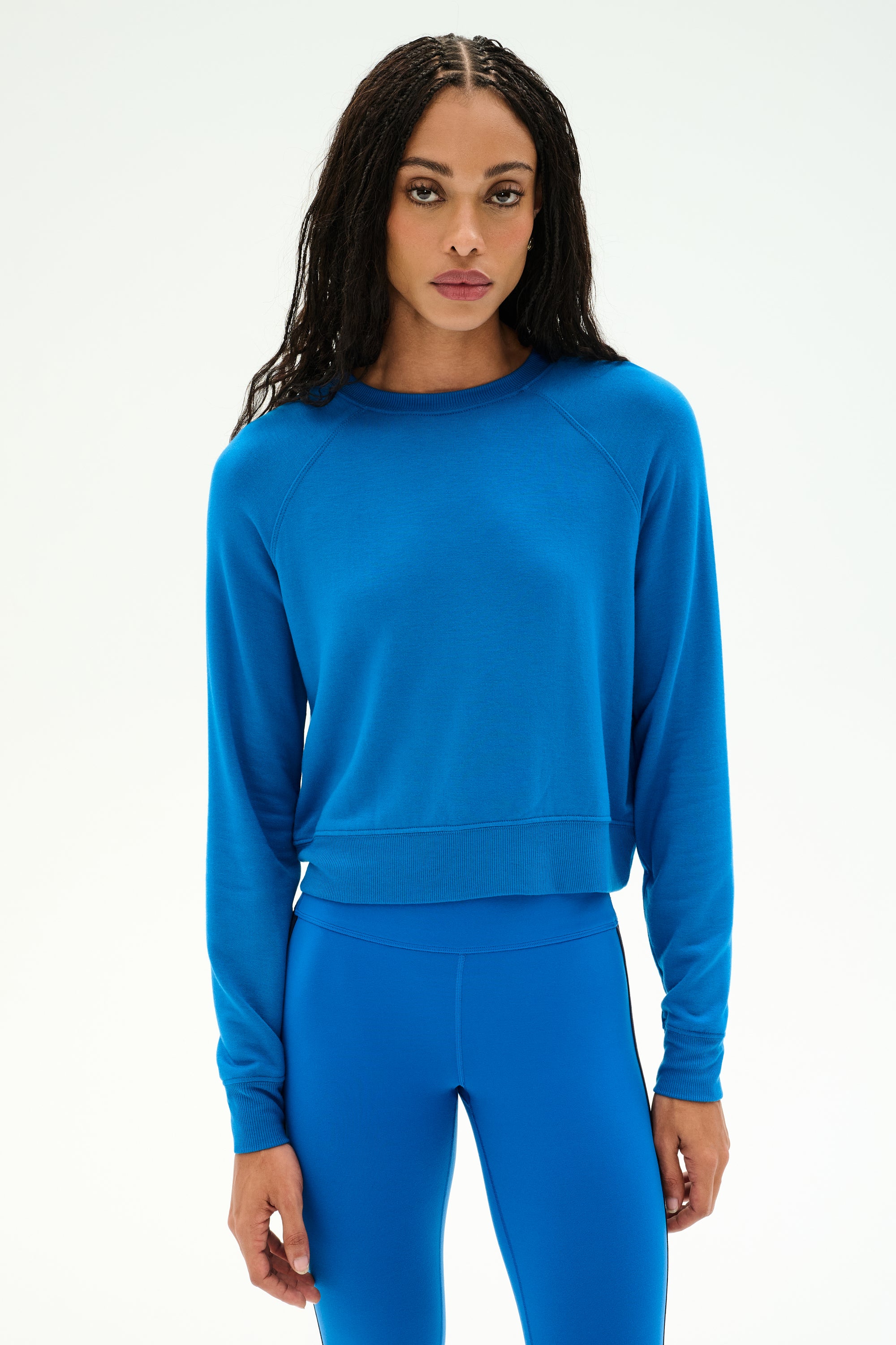 A woman wears the SPLITS59 Brooks Fleece Long Sleeve Sweatshirt in Classic Blue, paired with matching blue leggings, both crafted from a soft modal spandex blend, as she stands against a plain light background.