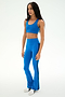 A woman stands on a white background wearing white sneakers and the SPLITS59 Raquel High Waist Supplex Flare 30" leggings in Classic Blue/Indigo, paired with a matching blue sports bra.