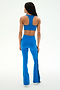 A woman stands with her back to the camera, modeling the SPLITS59 Raquel High Waist Supplex Flare in Classic Blue/Indigo—a pair of high-waisted workout pants featuring black side stripes, a flattering flared leg silhouette, and comfortable 4-way stretch—paired with a matching blue racerback sports bra, set against a plain white background.