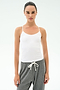 A woman wears the SPLITS59 Loren Seamless Waist Length Tank in white with gray sweatpants, standing facing forward against a plain white background.