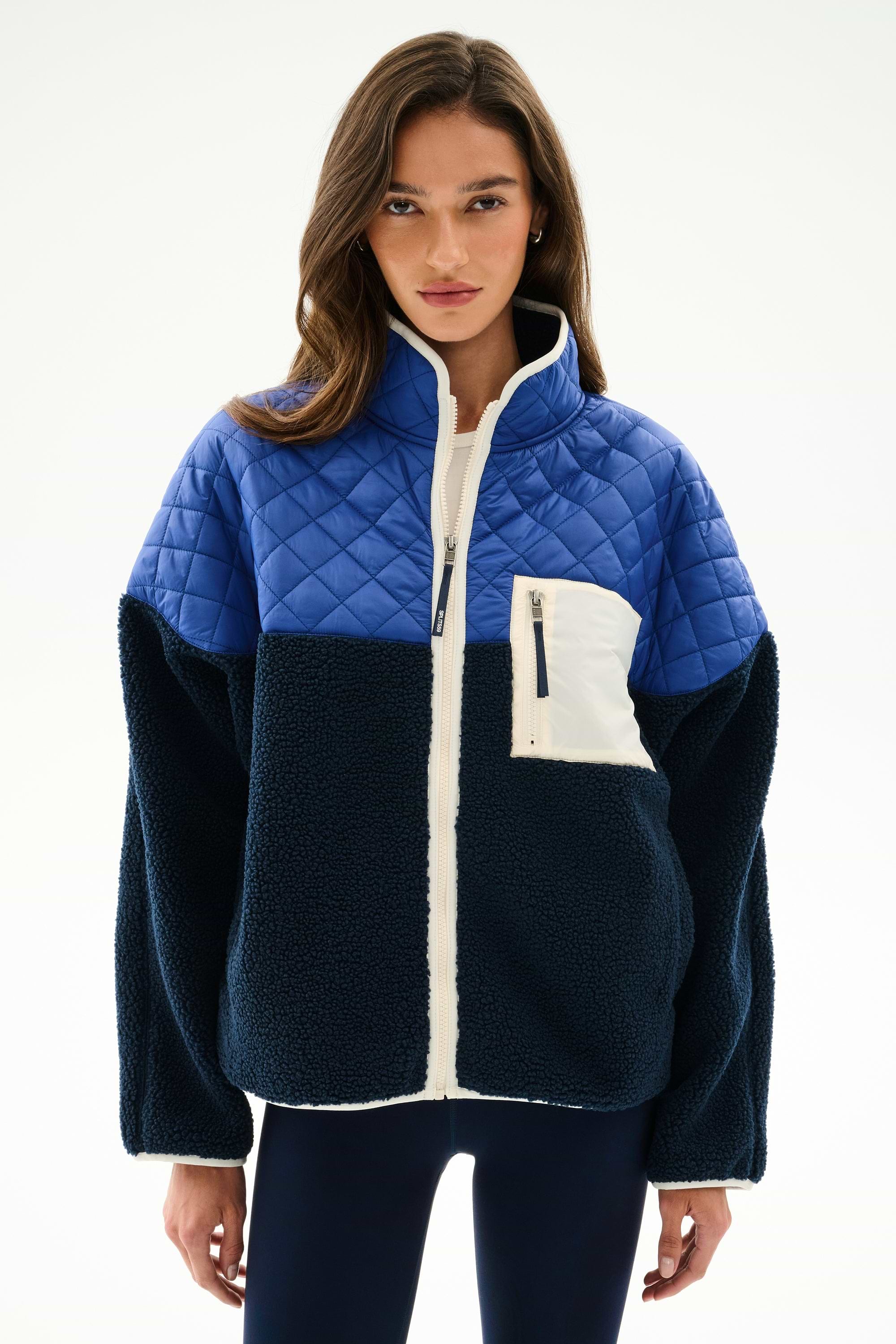Woman wearing the SPLITS59 Skylar Sherpa Jacket - Indigo/Cobalt, featuring quilted and sherpa panels, white zipper, and chest pocket, against a plain white background.
