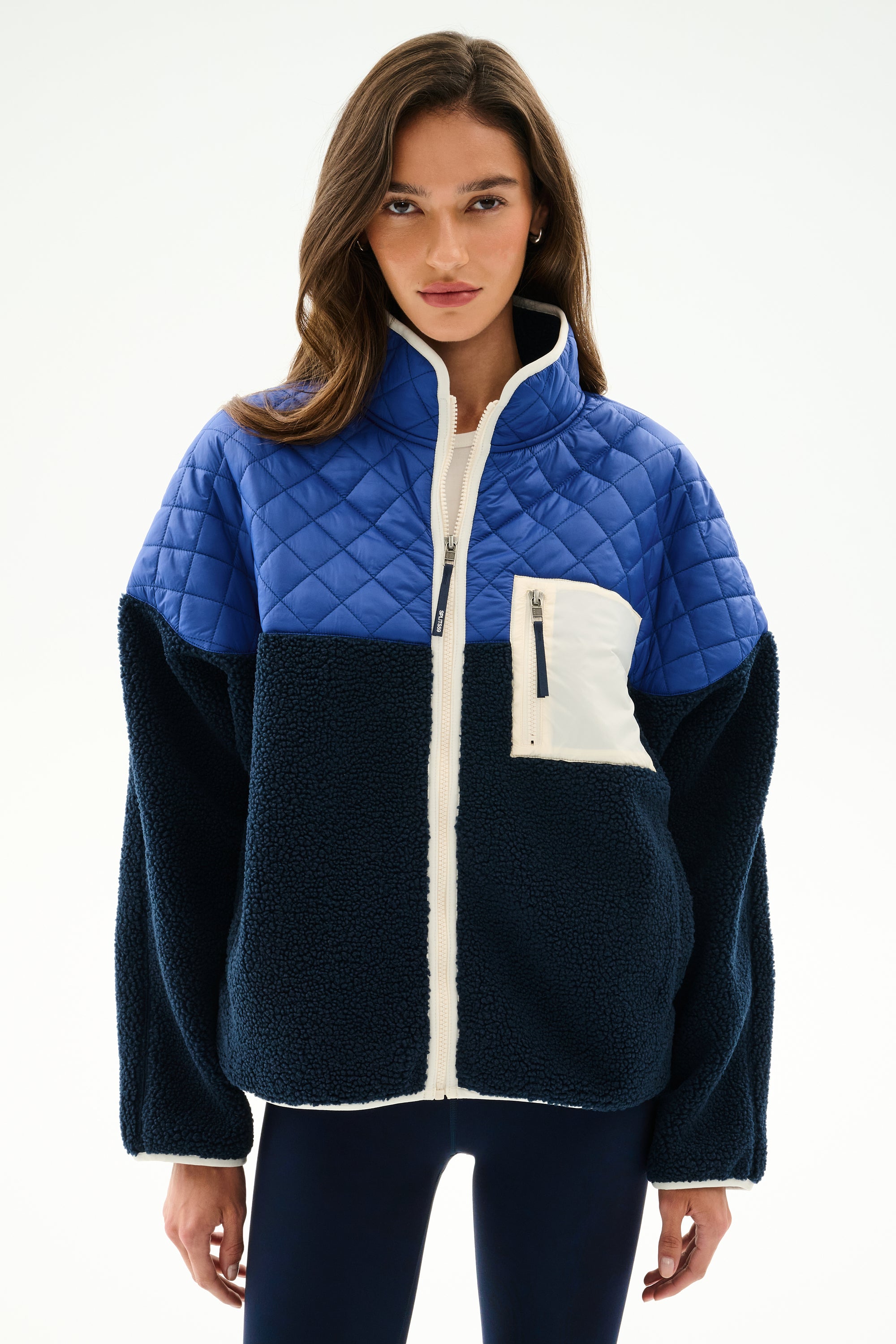 Woman wearing the SPLITS59 Skylar Sherpa Jacket - Indigo/Cobalt, featuring quilted and sherpa panels, white zipper, and chest pocket, against a plain white background.