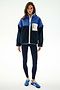 A woman faces forward wearing the SPLITS59 Skylar Sherpa Jacket - Indigo/Cobalt, navy leggings, and blue Adidas sneakers against a plain white background.