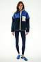 A woman faces forward wearing the SPLITS59 Skylar Sherpa Jacket - Indigo/Cobalt, navy leggings, and blue Adidas sneakers against a plain white background.