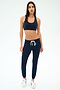 A woman stands against a plain background wearing a navy sports bra, SPLITS59 Sonja Fleece Sweatpant in Indigo with a white drawstring, and white sneakers.