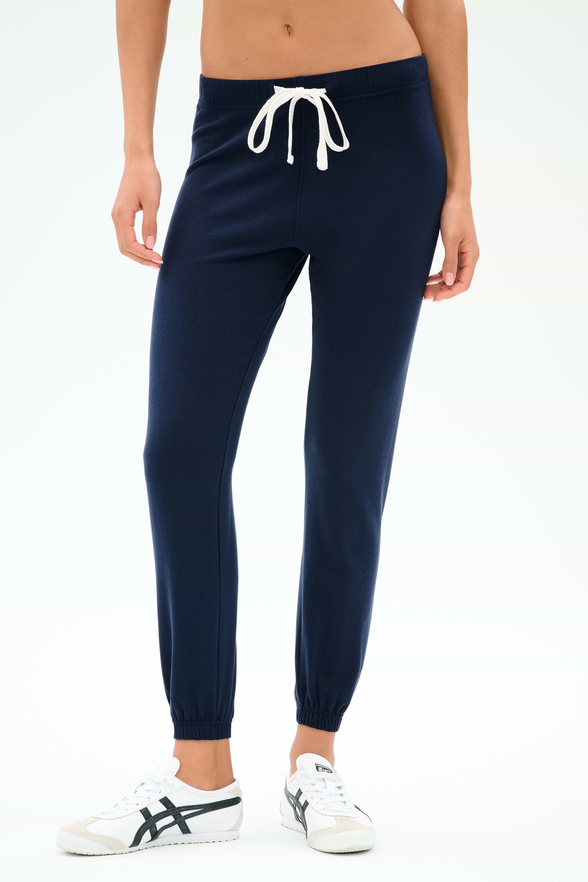 Model wears the SPLITS59 Sonja Fleece Sweatpant in Indigo—navy blue, slouchy-soft joggers with a white drawstring and white sneakers, crafted from ultra luxe fleece in Los Angeles—against a plain background.