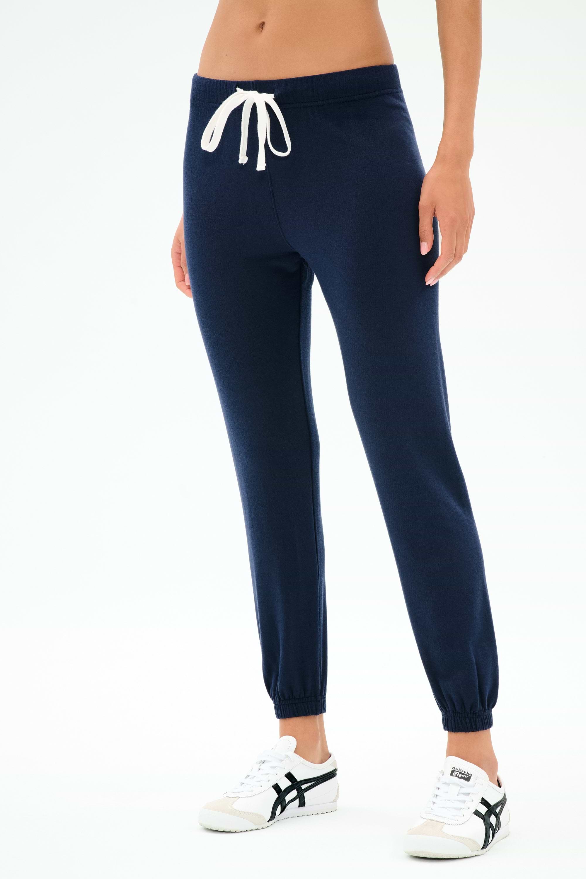 A person in SPLITS59 Sonja Fleece Sweatpant - Indigo, featuring slouchy-soft ultra luxe fleece and a white drawstring, paired with white sneakers, stands against a plain white background.