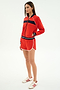 A woman wears the SPLITS59 Carrie Woven Nylon Jacket in Lotus Red/Indigo, paired with matching red spandex shorts trimmed in white and white sneakers featuring red stripes.