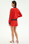 A woman faces away, wearing the SPLITS59 Carrie Woven Nylon Jacket in Lotus Red/Indigo and matching red spandex shorts with white trim, paired with white sneakers featuring red stripes, all set against a plain white background.