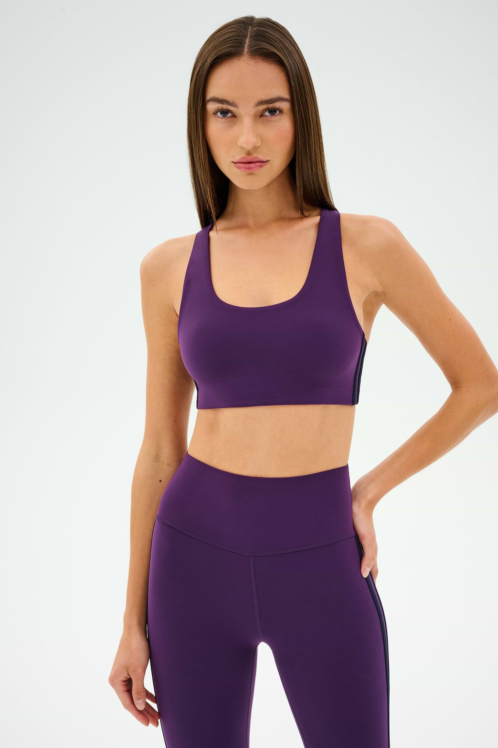 Wearing the SPLITS59 Ella Airweight Bra in Black Currant/Indigo, a person stands confidently against a plain background, ready for hot yoga.