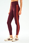 A person wears SPLITS59's Ella High Waist Airweight 7/8 leggings in Dark Cherry/Valencia with white sneakers featuring burgundy accents, standing against a plain background.