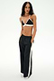 A person stands with hands in pockets, wearing a black nylon bralette, SPLITS59 Jordan Nylon Twill Tearaway pants in Black/Creme, and white sneakers against a plain white background.