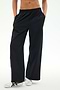 A person wearing the SPLITS59 Jordan Nylon Twill Tearaway track pants in Black/Creme, crafted from a lightweight nylon-spandex blend, stands with hands in pockets and white sneakers with black stripes against a plain background.