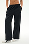 A person wearing the SPLITS59 Jordan Nylon Twill Tearaway track pants in Black/Creme, crafted from a lightweight nylon-spandex blend, stands with hands in pockets and white sneakers with black stripes against a plain background.