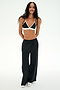 A person stands and smiles against a plain white background, wearing SPLITS59's Jordan Nylon Twill Tearaway pants in Black/Creme, paired with a black and white spandex bikini-style top and white shoes.