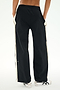 A person is seen from behind with hands in pockets, wearing SPLITS59's Jordan Nylon Twill Tearaway pants in Black/Creme, featuring white side stripes and crafted from a comfortable blend of nylon and spandex.