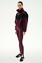 A woman stands against a plain white background, wearing the SPLITS59 Lottie Chevron Sherpa Full Zip Jacket in Dark Cherry/Black, paired with maroon leggings and black Adidas sneakers.