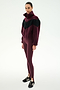 A woman stands against a plain white background, wearing the SPLITS59 Lottie Chevron Sherpa Full Zip Jacket in Dark Cherry/Black, paired with maroon leggings and black Adidas sneakers.