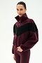 A person stands against a plain white background wearing the SPLITS59 Lottie Chevron Sherpa Full Zip Jacket in Dark Cherry/Black, crafted from soft 100% polyester fabric, paired with maroon leggings.