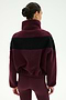 A person with dark hair in a bun is shown from the back against a plain background, wearing the SPLITS59 Lottie Chevron Sherpa Full Zip Jacket in Dark Cherry/Black—crafted from 100% polyester and featuring a black chevron stripe—paired with matching maroon leggings.