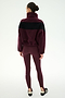 A woman stands facing away against a plain white background, wearing the SPLITS59 Lottie Chevron Sherpa Full Zip Jacket in Dark Cherry/Black—crafted from 100% polyester—with matching maroon leggings and black slip-on shoes.