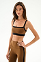 A woman poses with one hand on her hip, wearing the SPLITS59 Monah Rigor Bra - Toffee/Black and matching leggings against a white background.