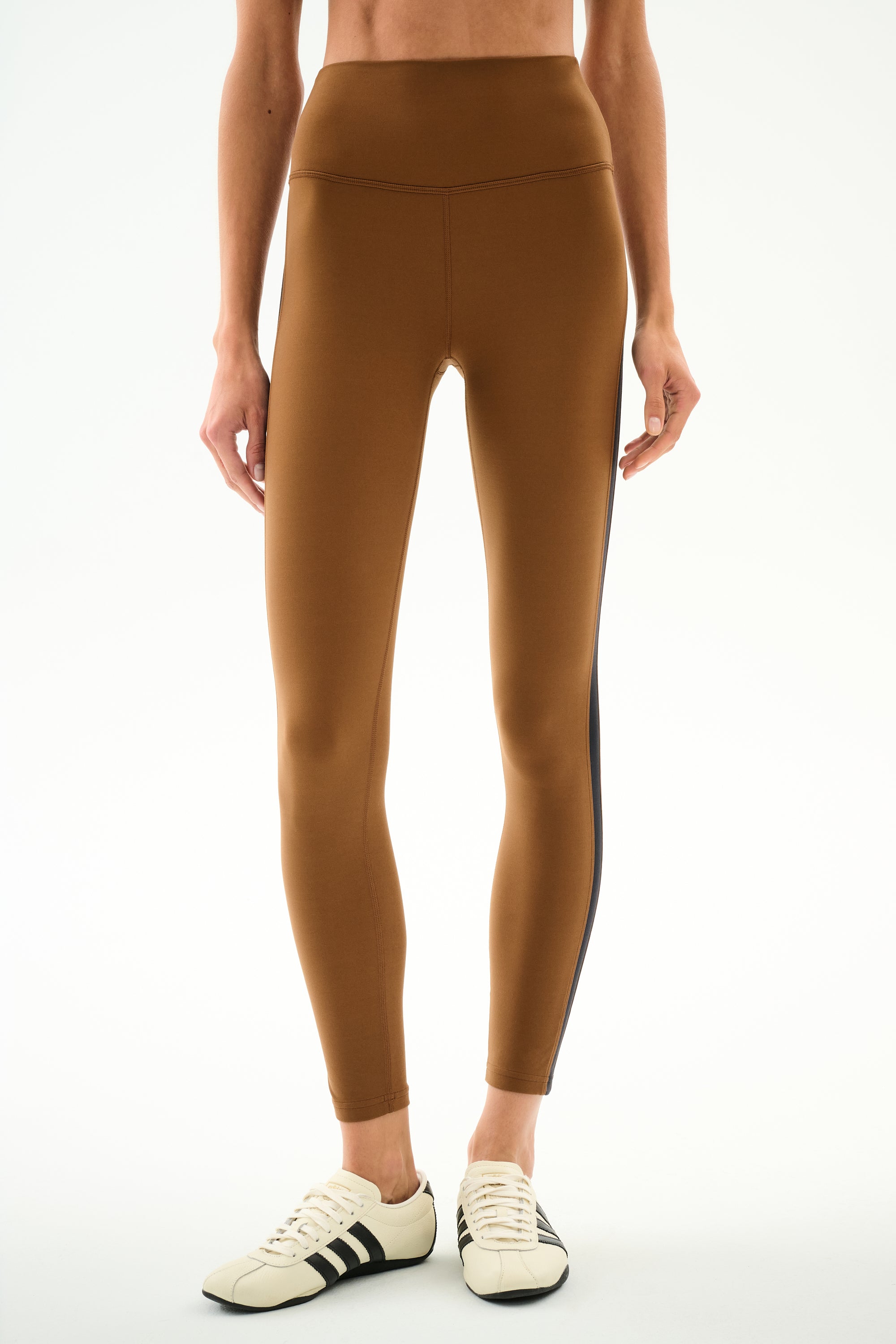 Model wears SPLITS59 Clare High Waist Rigor 7/8 - Toffee/Black with white sneakers featuring black stripes, standing against a plain background.