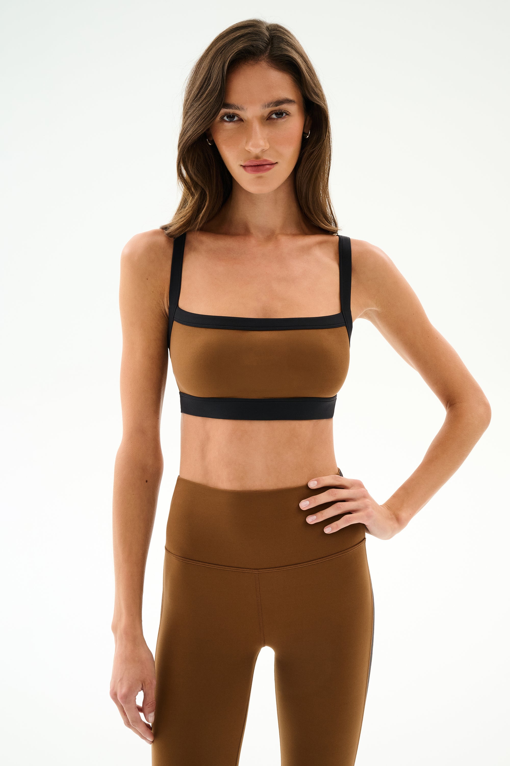 Woman poses with one hand on hip, wearing the SPLITS59 Monah Rigor Bra - Toffee/Black with matching high-waisted leggings against a plain white background.