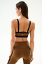 A woman faces away wearing the SPLITS59 Monah Rigor Bra - Toffee/Black with matching high-waisted leggings against a plain background.