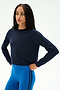 A woman stands with her hands on her hips against a plain light background, wearing the SPLITS59 Brooks Fleece Long Sleeve Sweatshirt in Indigo—a raglan sleeve crewneck pullover. She pairs it with bright blue athletic leggings featuring black stripes for a stylish look made in Los Angeles.