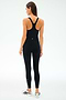A woman stands facing away, wearing the SPLITS59 Ella High Waist Airweight 7/8 leggings in Black/White and a black racerback tank top, paired with white sneakers—ideal attire for hot yoga sessions against a plain light background.