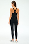 A woman stands facing away, wearing the SPLITS59 Ella High Waist Airweight 7/8 leggings in Black/White and a black racerback tank top, paired with white sneakers—ideal attire for hot yoga sessions against a plain light background.