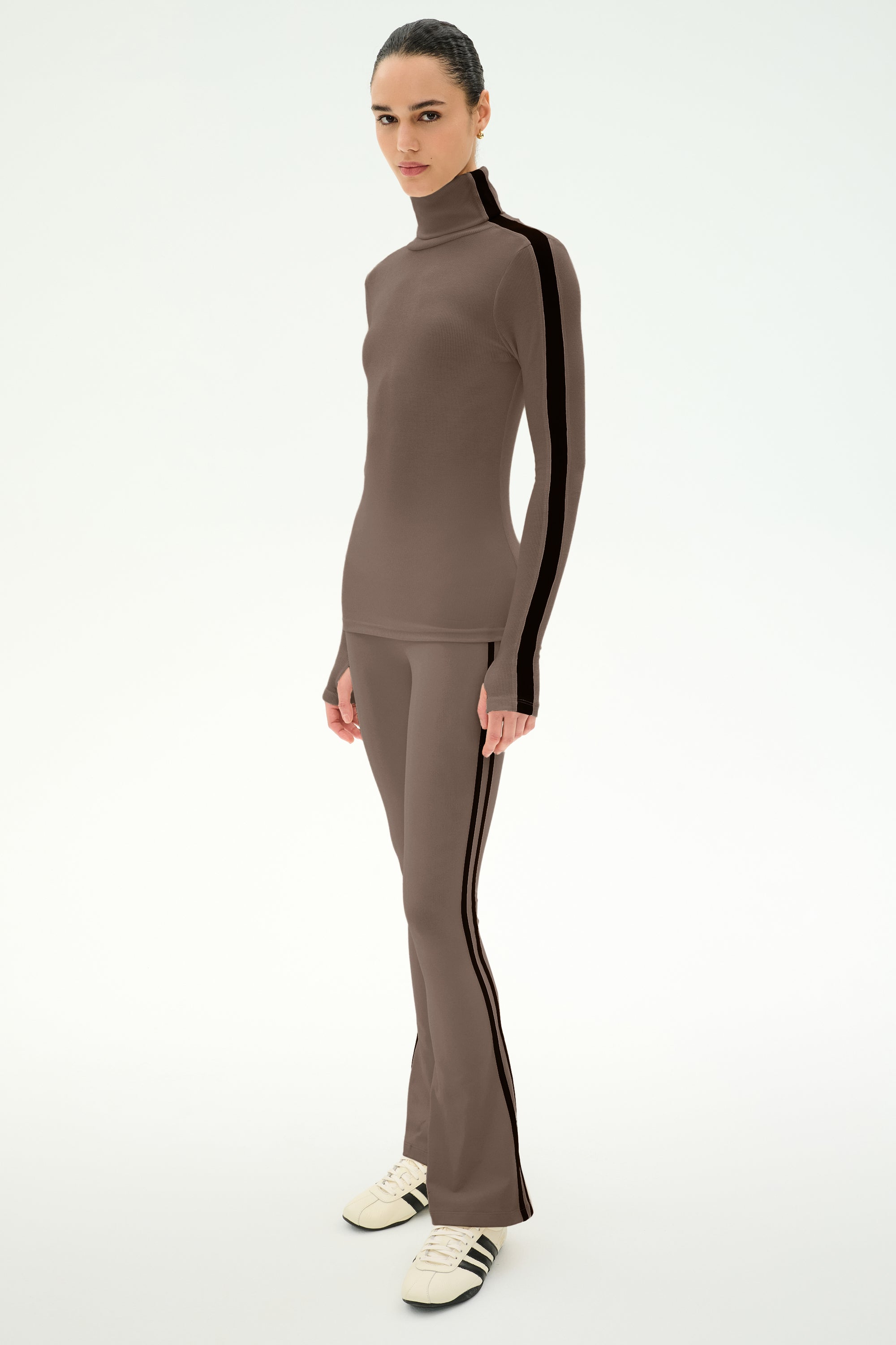 A person wearing the SPLITS59 Raquel High Waist Supplex Flare pants in Lentil/Black, featuring black side stripes and crafted from a smooth nylon-spandex blend, stands against a plain white background.