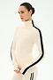 A woman wearing the SPLITS59 Jackson Rib Full Length Turtleneck in Creme/Black, featuring black stripes down the sleeves and crafted from a soft modal blend for added comfort, stands against a plain white background.