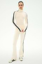 A person stands against a plain white background wearing the SPLITS59 Jackson Rib Full Length Turtleneck in Creme/Black, paired with matching flare pants featuring black side stripes and cream and black sneakers.