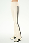 A person is wearing the SPLITS59 Raquel High Waist Supplex Flare pants in Creme/Black—high-waisted, cream flared pants featuring two black side stripes—paired with cream sneakers with black stripes, standing on a plain background. Crafted from 4-way stretch Supplex fabric, these pants deliver comfort and flexibility, making them ideal for a casual day out or light workouts.