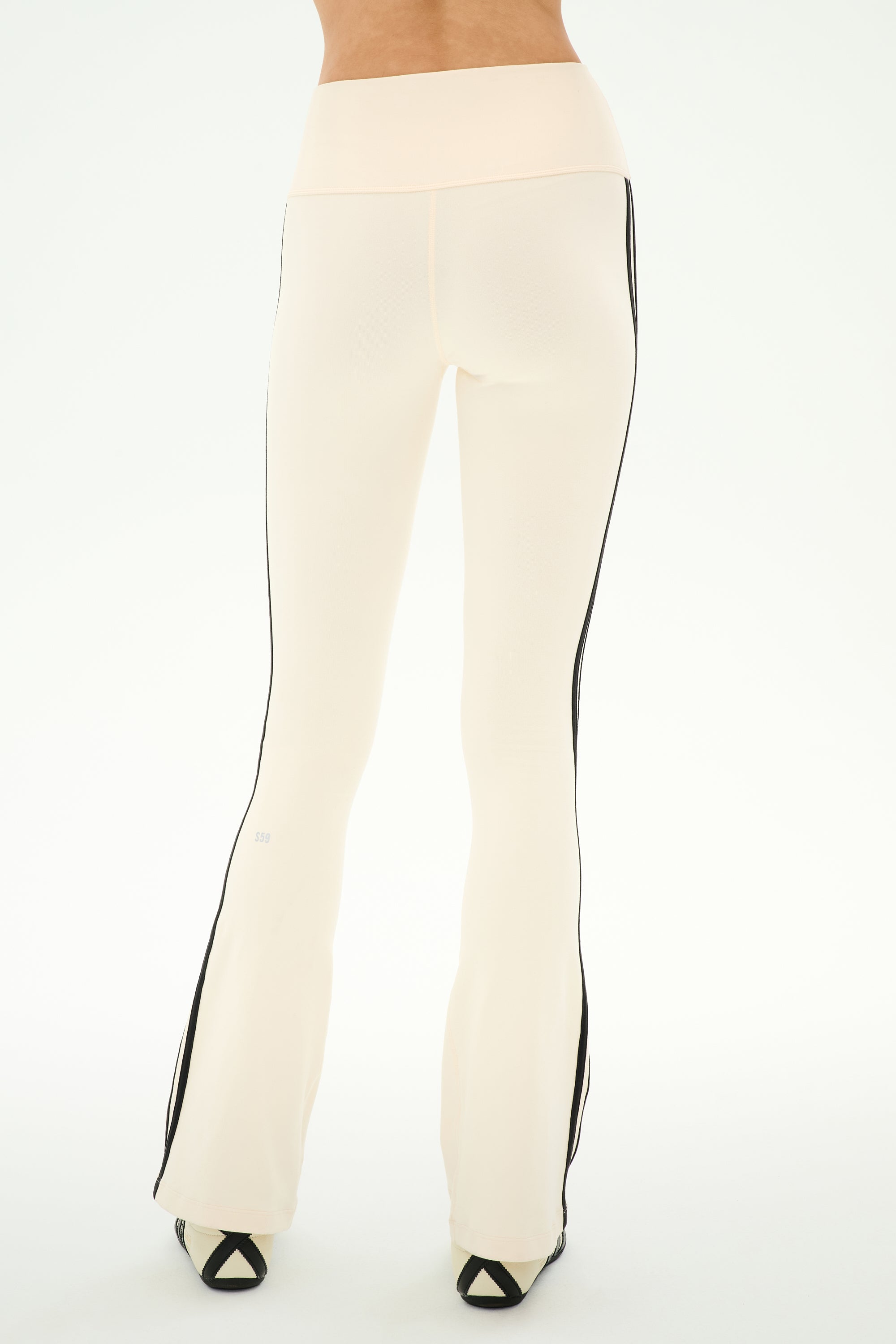 A model is shown from the back wearing the SPLITS59 Raquel High Waist Supplex Flare leggings in Creme/Black, featuring a high-rise fit, black side stripes, and 4-way stretch, standing against a white background.