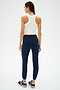 A person stands with their back to the camera, wearing a Kiki Rib Crop Tank in white from SPLITS59, navy joggers, and black sneakers against a plain white background.