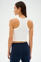 Seen from behind, a woman with long dark hair wears the Kiki Rib Crop Tank in white by SPLITS59 paired with dark blue pants.