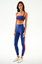 Woman wears SPLITS59 Clare High Waist Rigor 7/8 - Cobalt/Terracotta leggings and a matching top with white sneakers, standing against a white background.