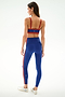 A woman faces away, wearing the Monah Rigor Bra - Cobalt/Terracotta by SPLITS59, in blue with red accents and white sneakers, on a plain white background.